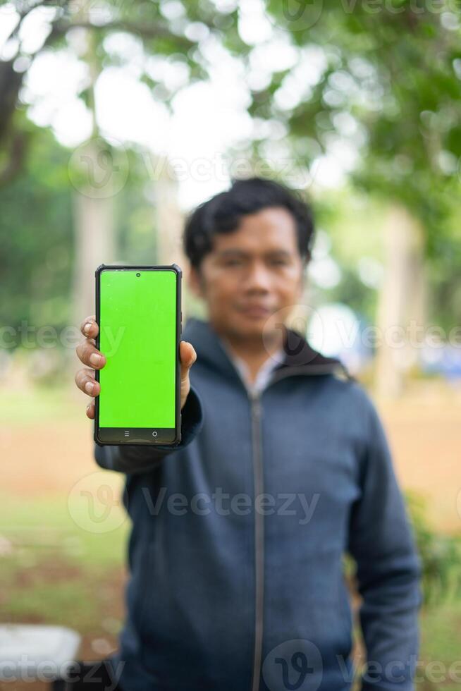 Southeast Asian man showing something on his smartphone with a green screen, perfect for customizable content photo