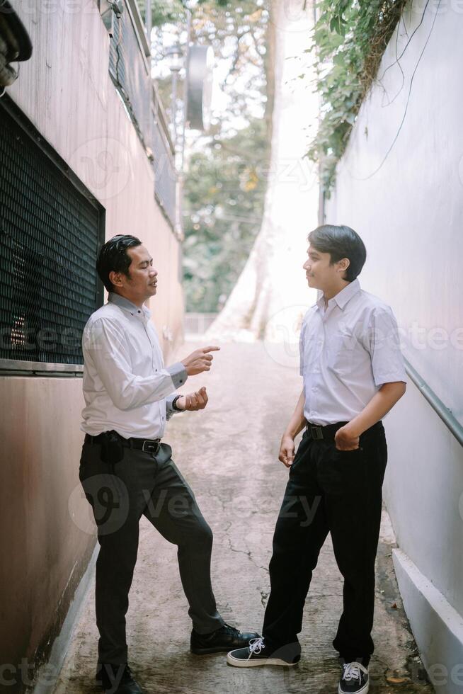Two Southeast Asian businessmen engaged in a business discussion outdoors, standing in a professional setting photo