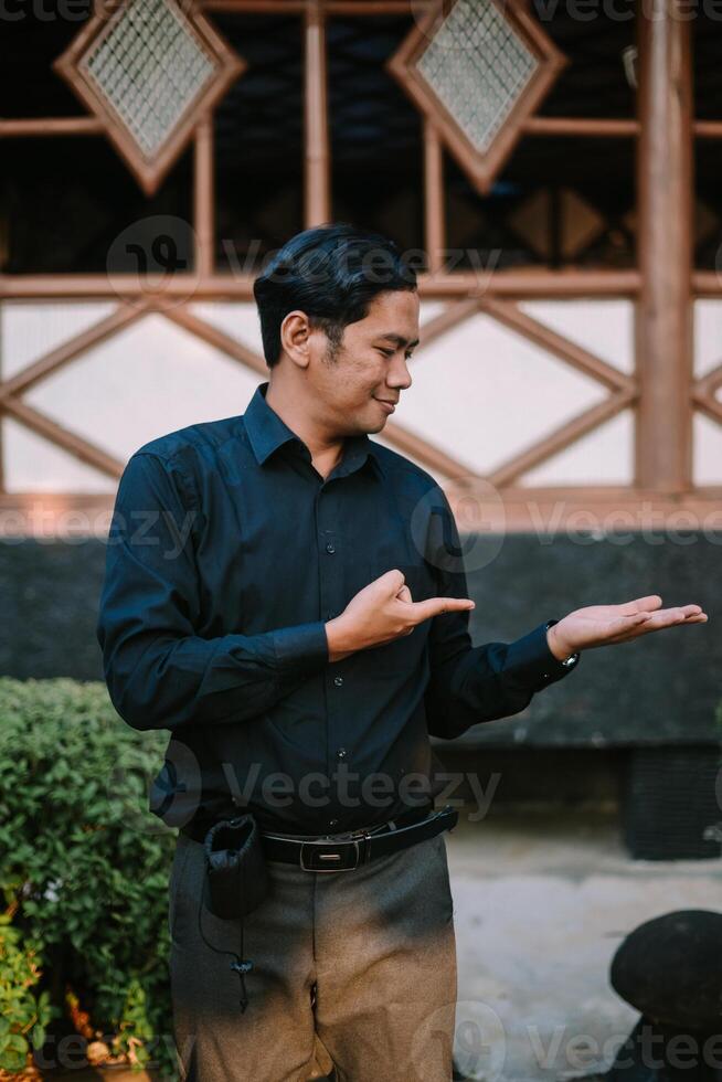 Southeast Asian man explaining something while gesturing toward an object in his hand, showcasing engagement and focus. photo