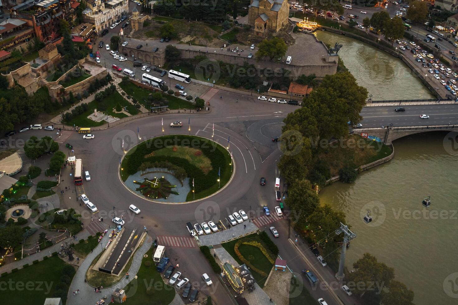 A bustling urban roundabout overlooking a serene river in the heart of the city at dusk photo