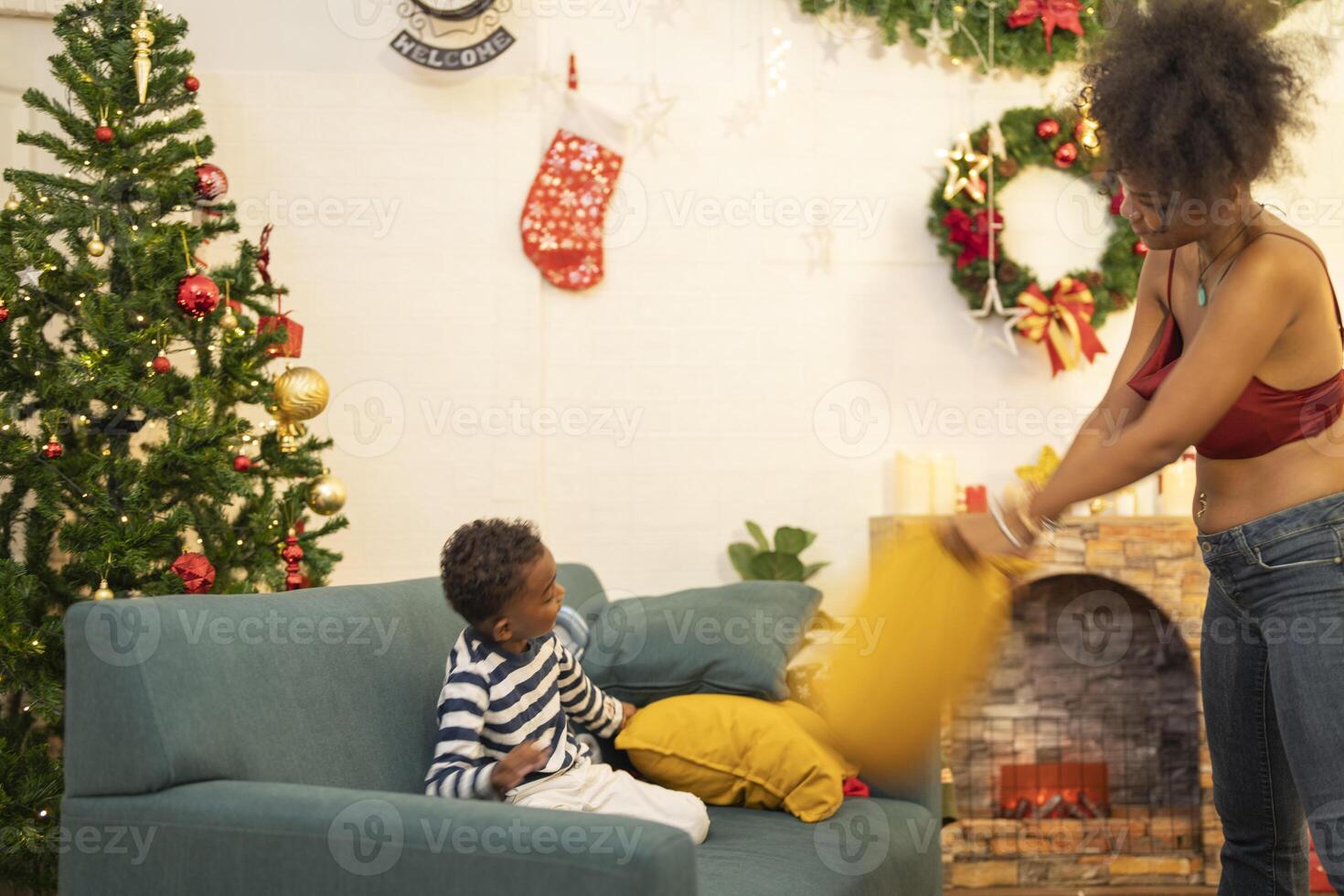 mother in a festive setting with a beautifully Christmas tree engages playfully with her child, who is lying on couch. The joyful atmosphere highlights holiday family bonding, home celebrations. photo