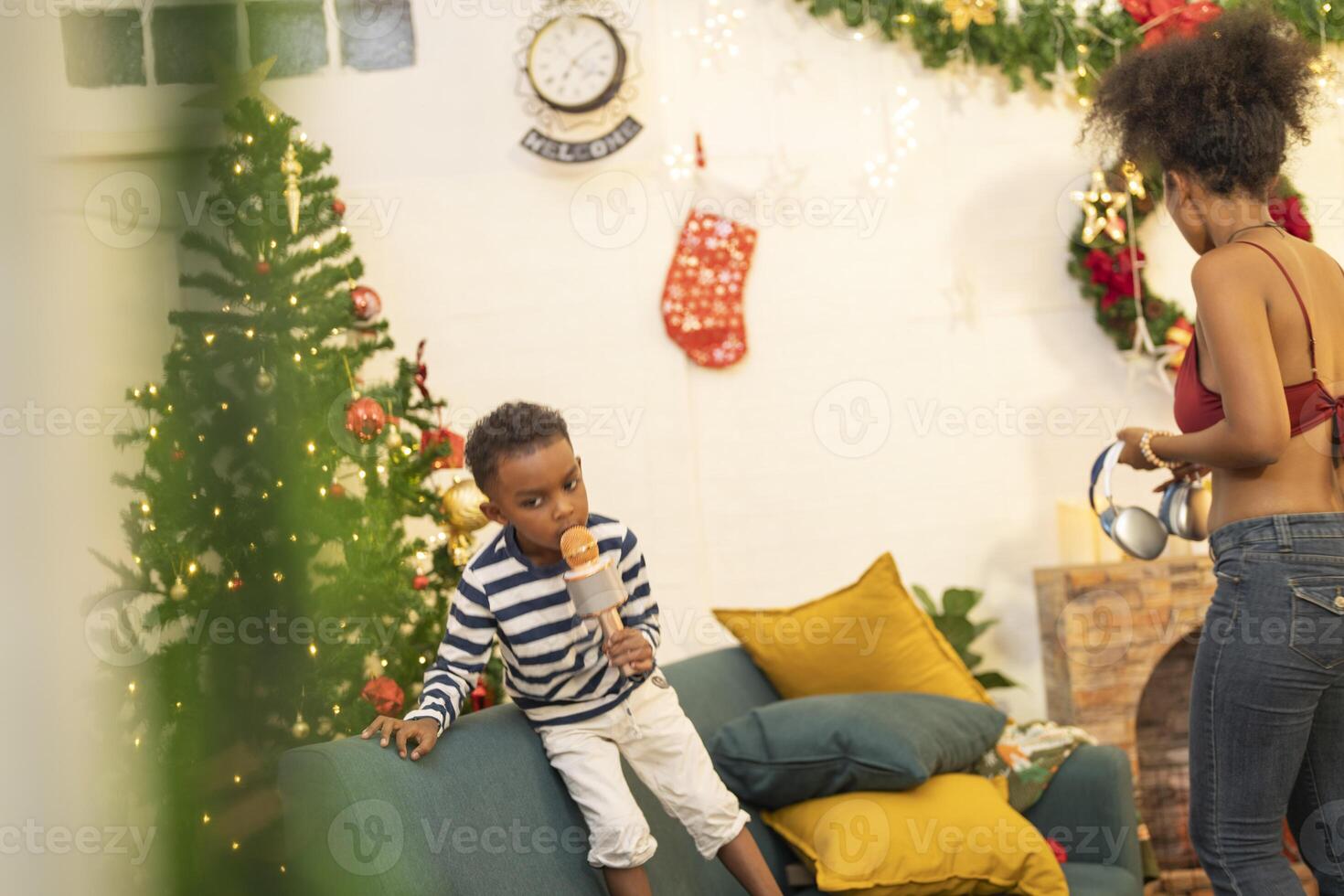 mother in a festive setting with a beautifully Christmas tree engages playfully with her child, who is lying on couch. The joyful atmosphere highlights holiday family bonding, home celebrations. photo