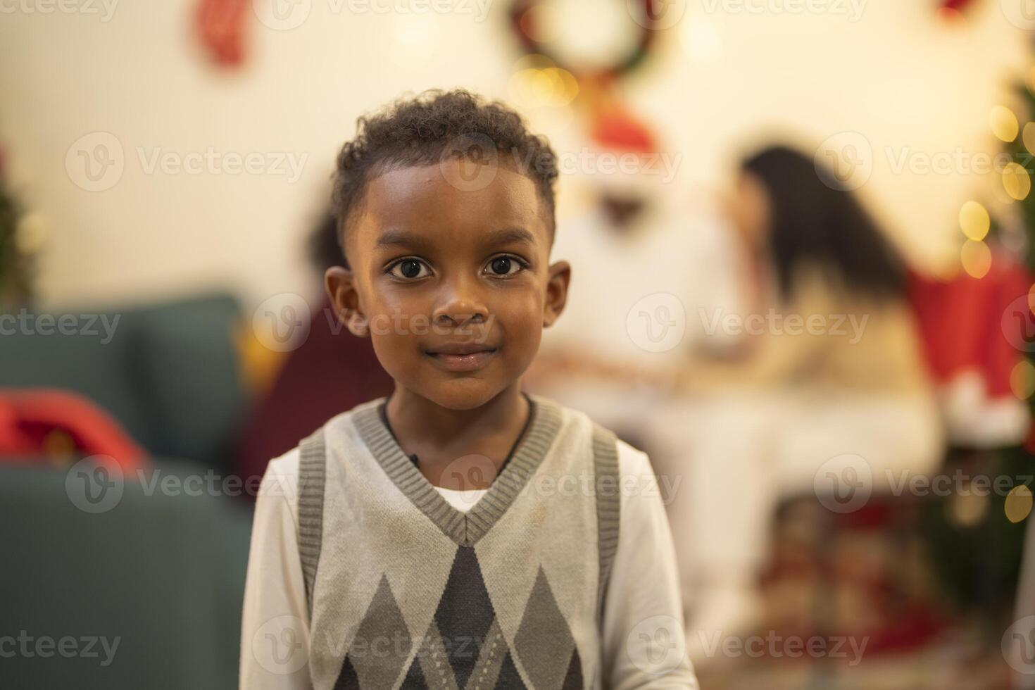 A close up portrait of a young boy smiling during a festive Christmas gathering. The soft bokeh from holiday lights and decorations in the background creates a warm and joyful atmosphere. photo