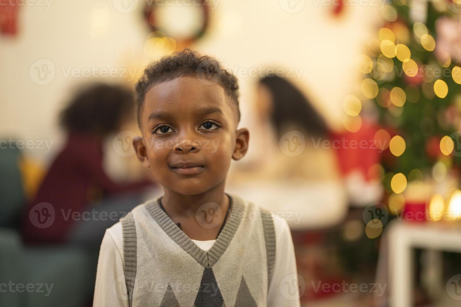 A close up portrait of a young boy smiling during a festive Christmas gathering. The soft bokeh from holiday lights and decorations in the background creates a warm and joyful atmosphere. photo