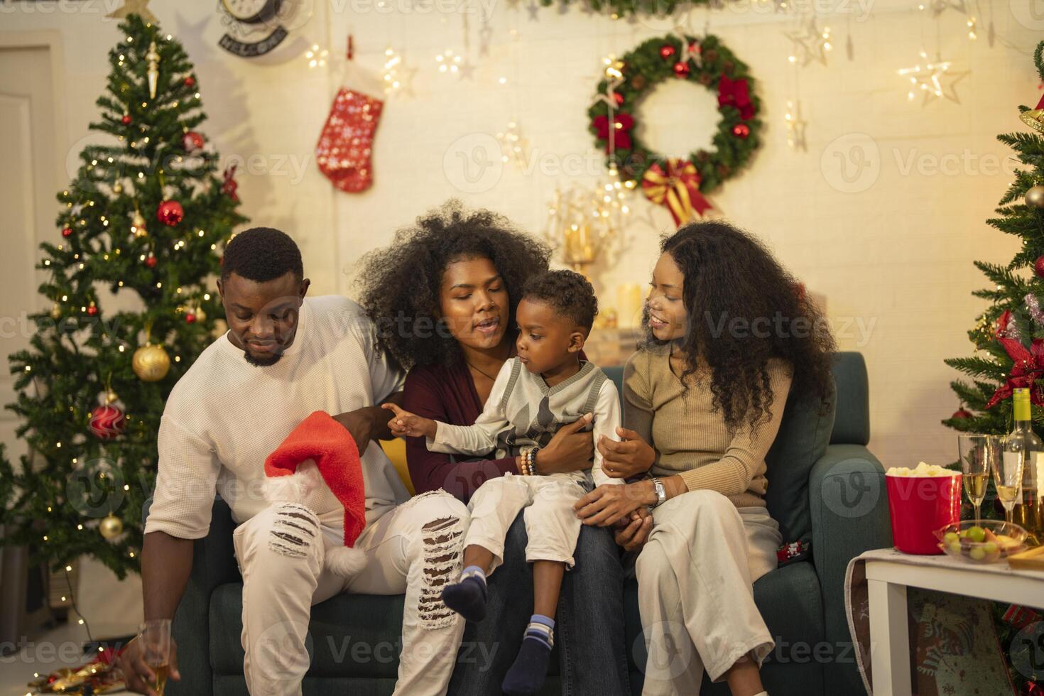 A lively Christmas celebration with three african friends enjoying drinks and holiday cheer on a sofa. The festive atmosphere includes Christmas trees, wreaths, lights, and decorations. photo