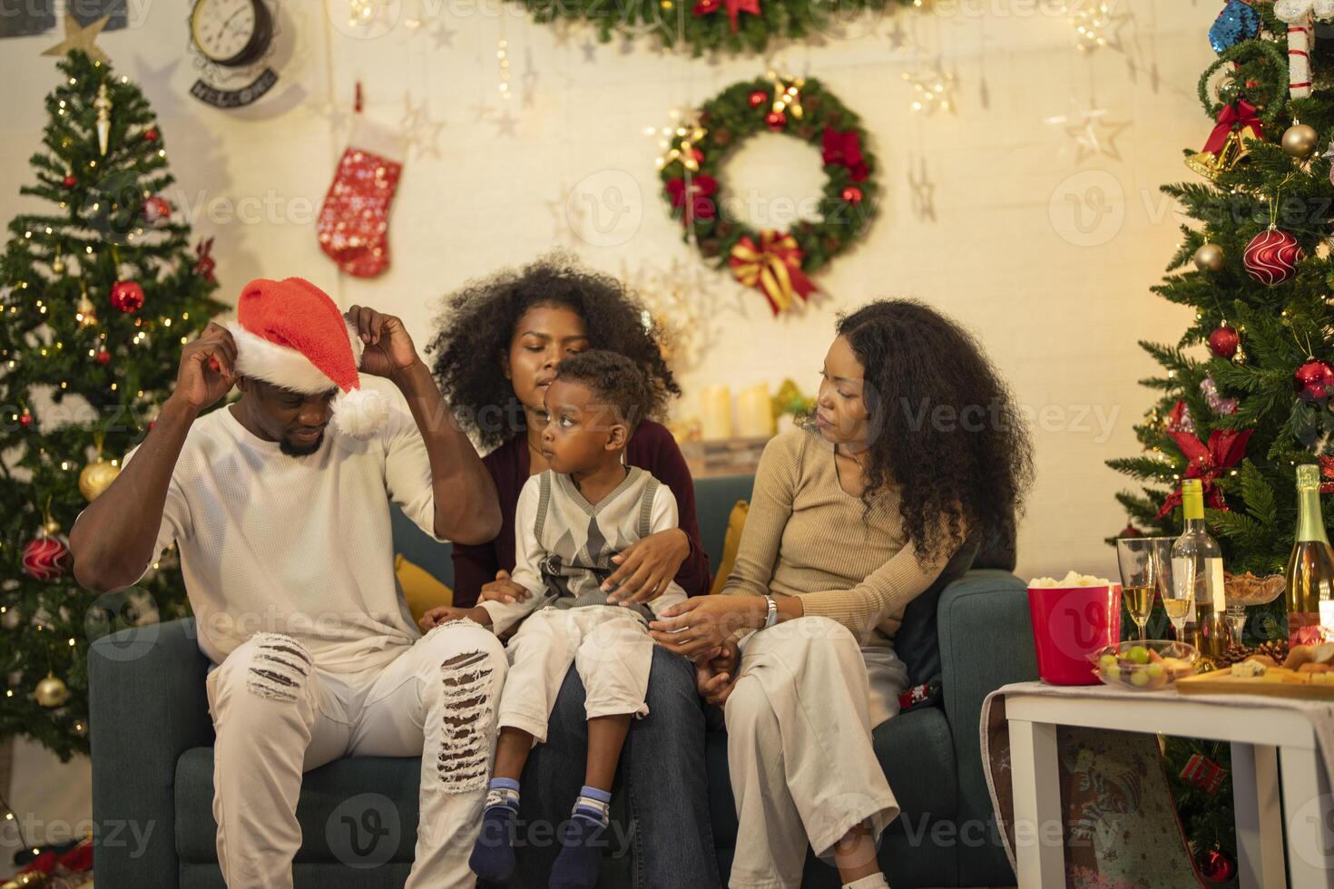 A lively Christmas celebration with three african friends enjoying drinks and holiday cheer on a sofa. The festive atmosphere includes Christmas trees, wreaths, lights, and decorations. photo