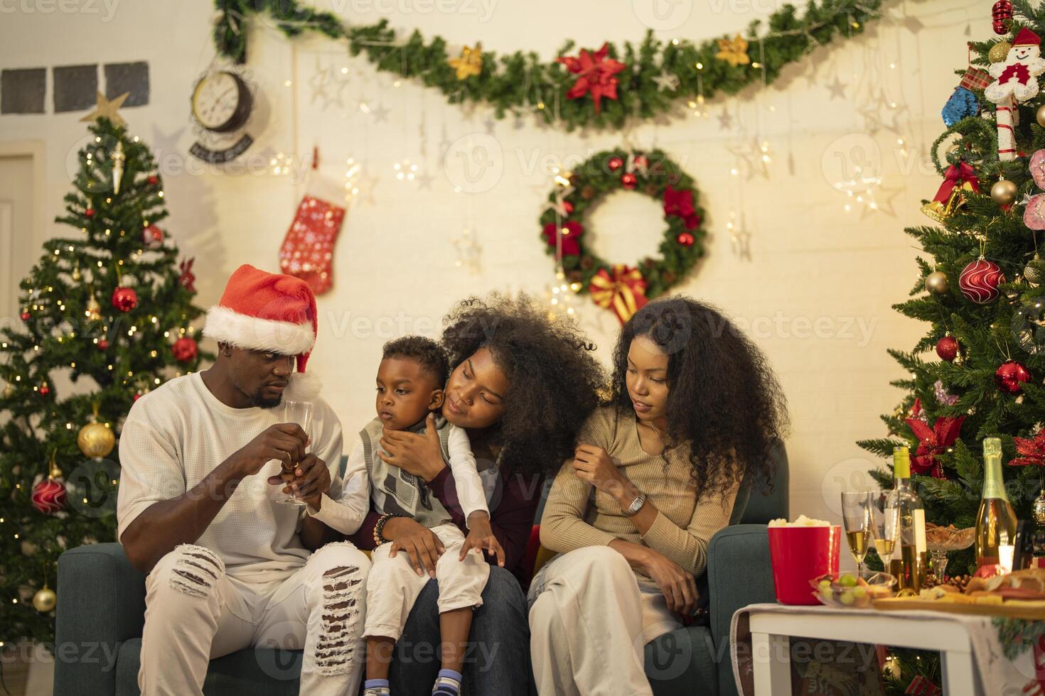 A lively Christmas celebration with three african friends enjoying drinks and holiday cheer on a sofa. The festive atmosphere includes Christmas trees, wreaths, lights, and decorations. photo