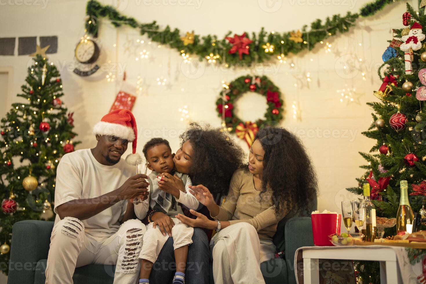 A lively Christmas celebration with three african friends enjoying drinks and holiday cheer on a sofa. The festive atmosphere includes Christmas trees, wreaths, lights, and decorations. photo