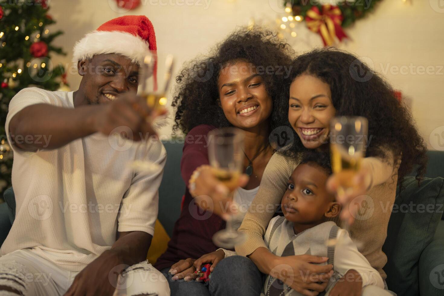 A lively Christmas celebration with three african friends enjoying drinks and holiday cheer on a sofa. The festive atmosphere includes Christmas trees, wreaths, lights, and decorations. photo