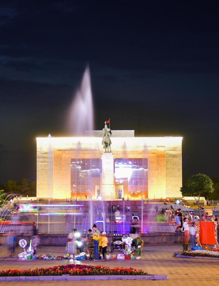 Bishkek, Kyrgyzstan - 25th september, 2023- tourist visit Manas Statue in Ala-Too Square. State history museum and fountain with tourist in city square. Sunset blue hour sky background photo