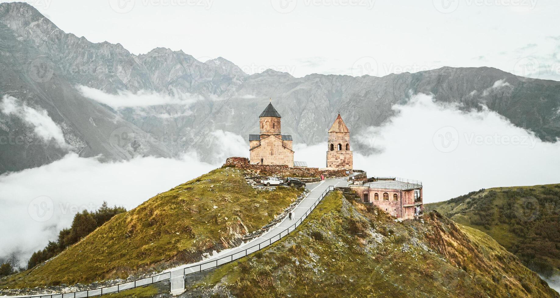 Aerial view Gergeti trinity church after sunset, Georgia. Stepanstminda famous sightseeing landmark on hilltop with misty caucasus mountains background. Tourist visit popular sightseeing attraction photo