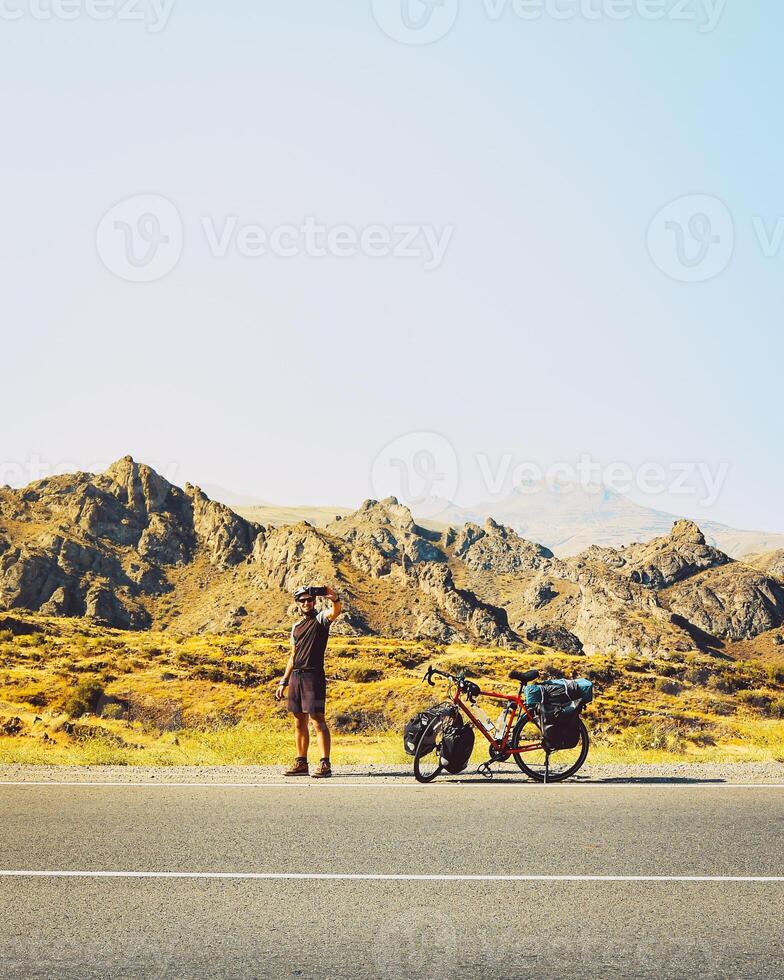 Cinematic travel inspirational panorama traveler cyclist stand on road take smiley self-portrait with mobile phone. Solo travel bicycle touring around the world photo