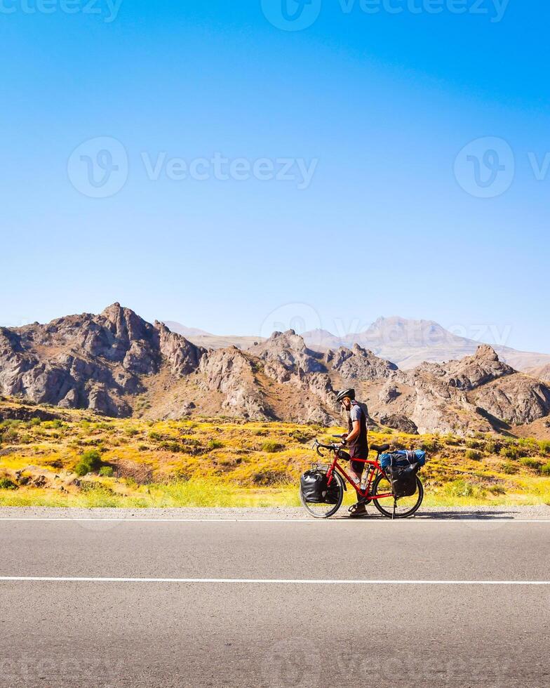 Solo cyclist on road with bicycle check map being lost outdoors in hot sunny day in deserted wilderness. Sportsman cyclist check phone on side of road. Vertical background photo