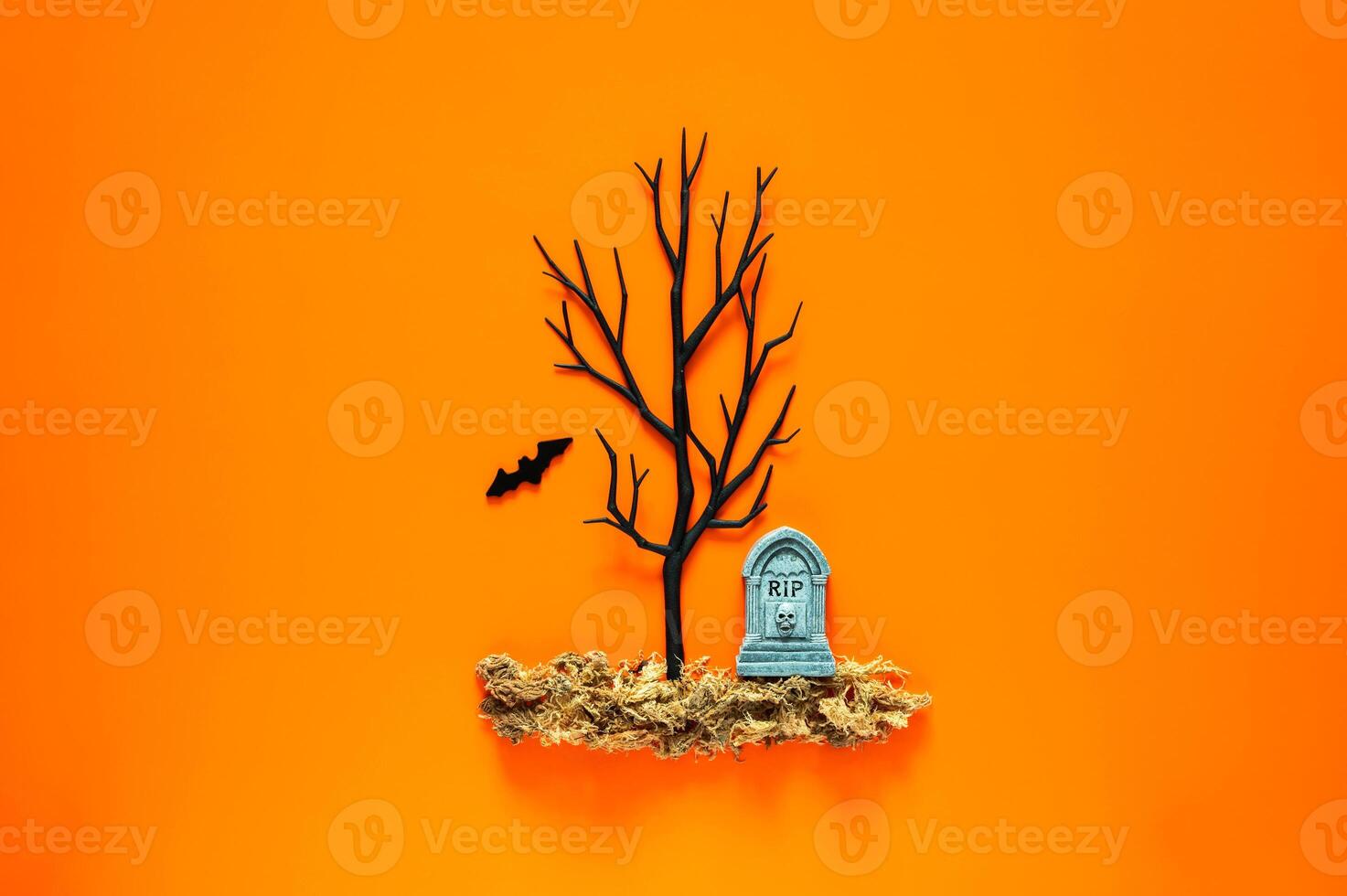 Halloween background with tombstone on dried grass and black tree with a bat on orange background. Minimal concept. photo