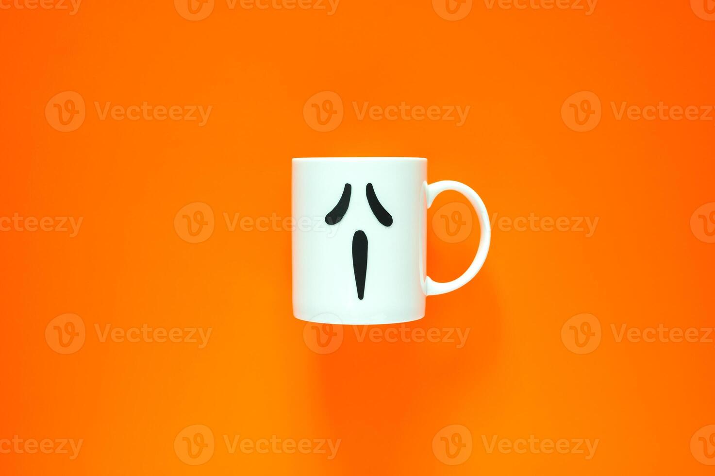 Halloween background with a coffee cup with eye and mouth stickers puts on orange background. Minimal concept. photo
