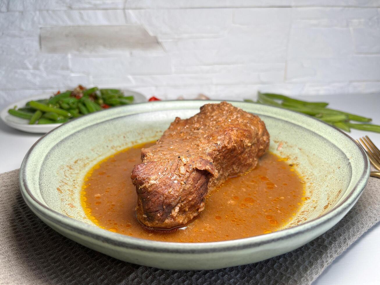 Delicious beef stewed with herbs and spices in a plate on the table with stir fry green beans. Slow cooked beef. photo