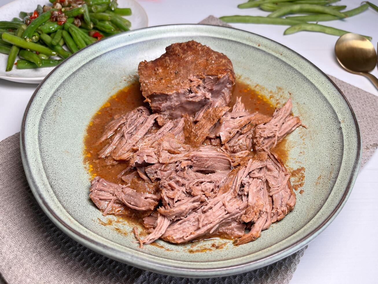 Pulled beef. Juicy and tender beef stewed with herbs and spices in a plate and stir fry green beans on the table. Slow cooked beef. photo