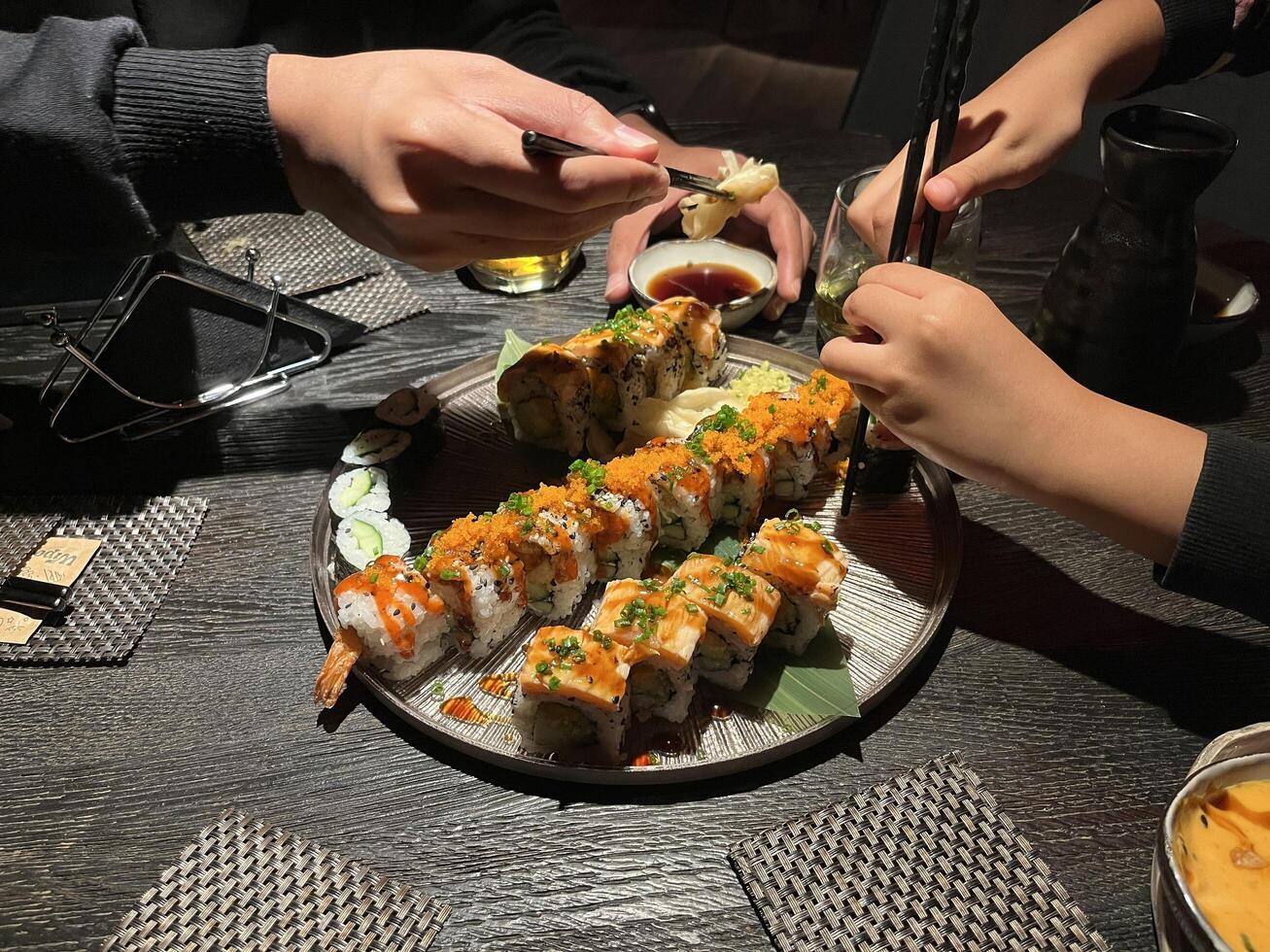 Unrecognized man and unrecognized little girl hand's using chopsticks to pick up pieces of sushi from a large platter, which includes various types of rolls and nigiri. photo