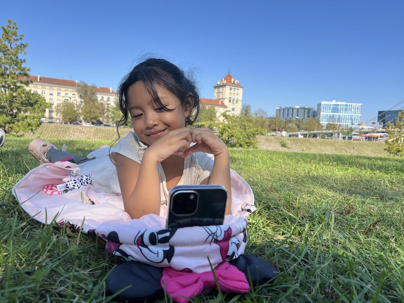 Smiling Asian little girl on the grass using phone in outdoor making call with love sign hand gesture photo