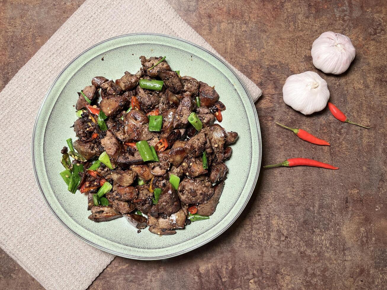 Tumis Ati Goreng is a popular Indonesian stir-fried chicken liver dish known for its rich, savory flavors and spicy kick served on a plate with rustic background. Top view photo