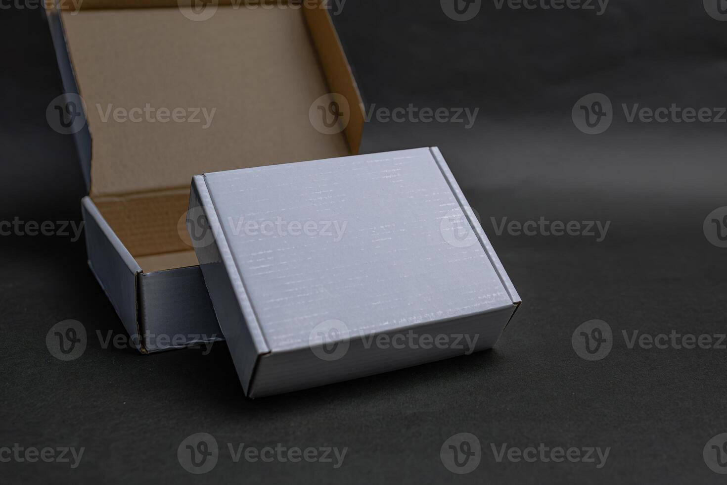 A white box is sitting on top of a brown box The white box is slightly open The white box is sitting on a black surface photo