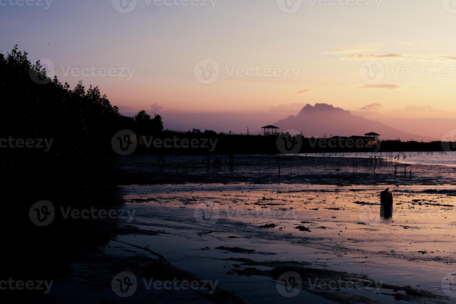 A silhouette of a mountain range and trees at sunset over a shore photo