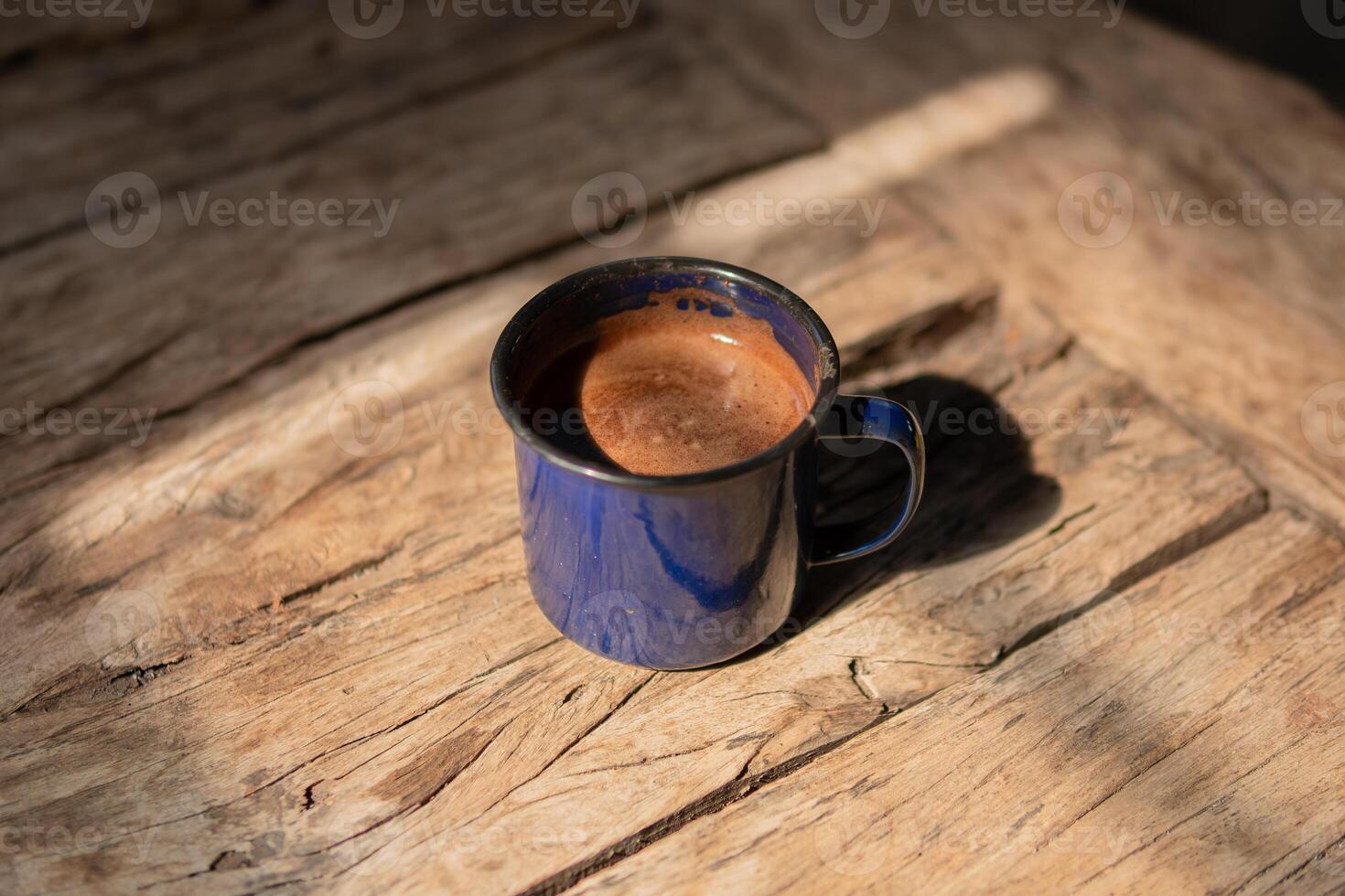 A blue mug of coffee sits on a wooden surface with a shadow from the window photo