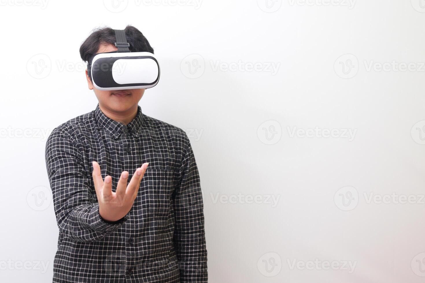 Portrait of Asian man in black plaid shirt using Virtual Reality VR glasses and trying to hold something in front of him. Isolated image on white background photo