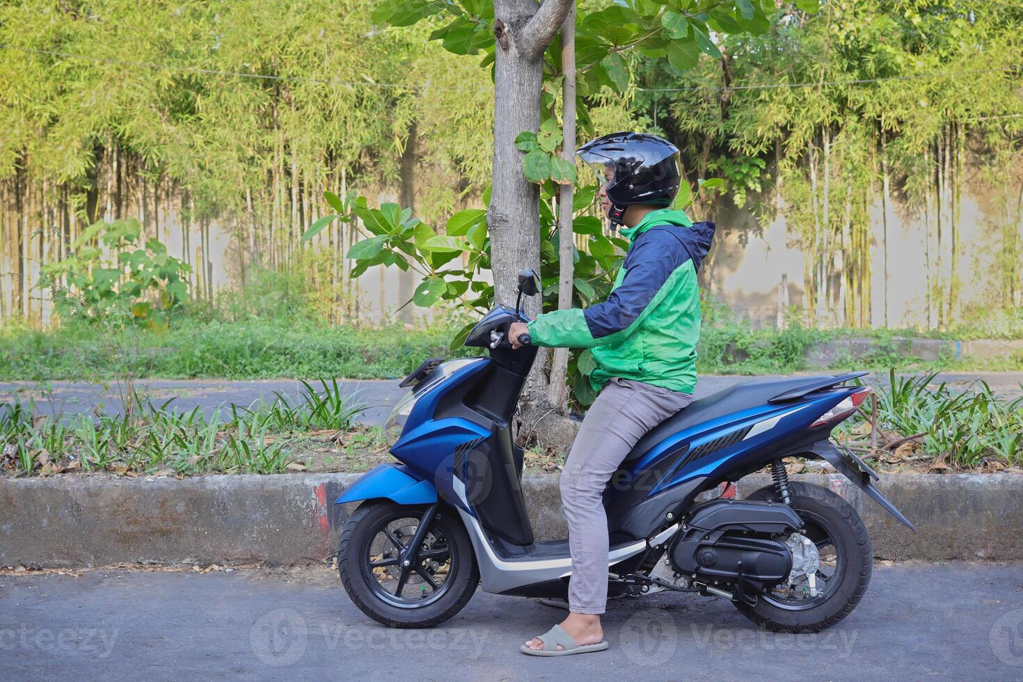 Side view of online taxi rider wearing green jacket and helmet, riding motorcycle while on the way to pick up customer. Transportation application concept. photo