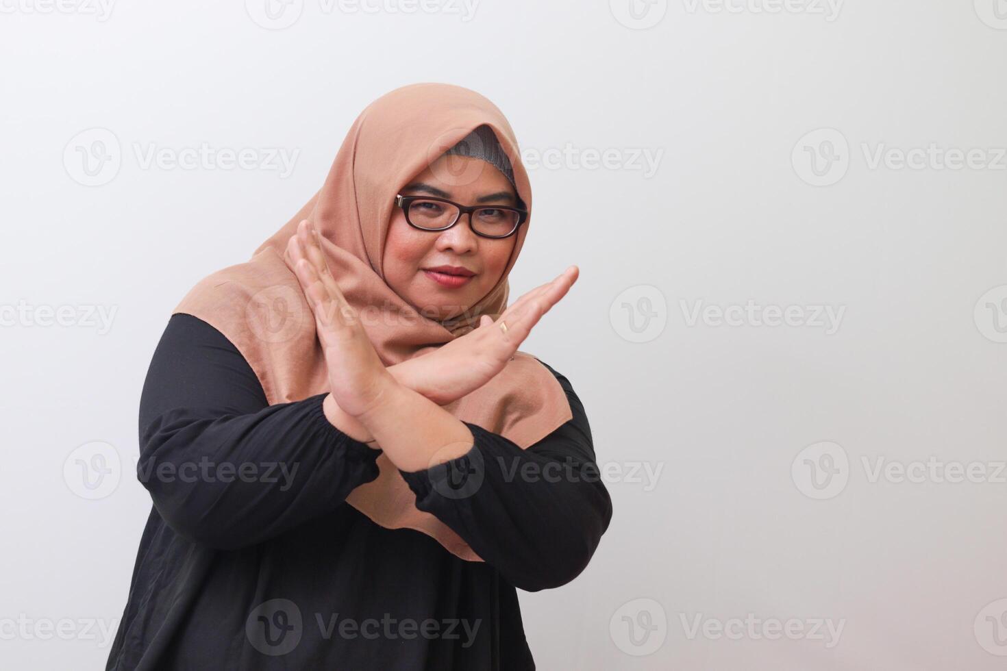 Portrait of serious Asian woman with hijab, showing X sign of hands for refusing an invitation from someone. Isolated image on white background photo