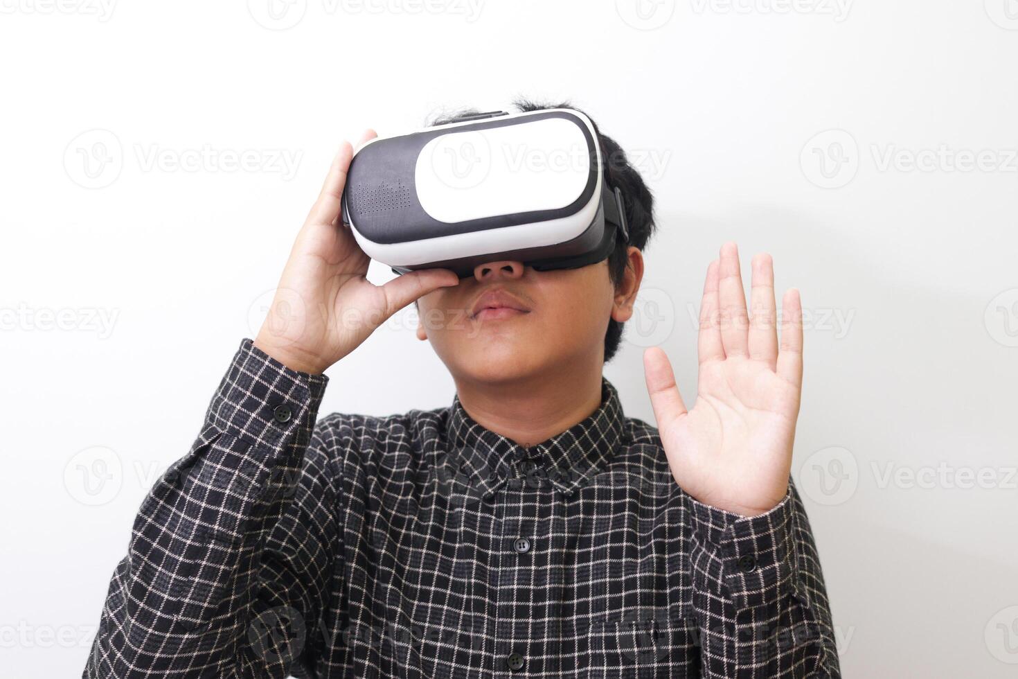 Portrait of Asian man in black plaid shirt using Virtual Reality VR glasses and greet his friend inside the game with opened palm. Isolated image on white background photo