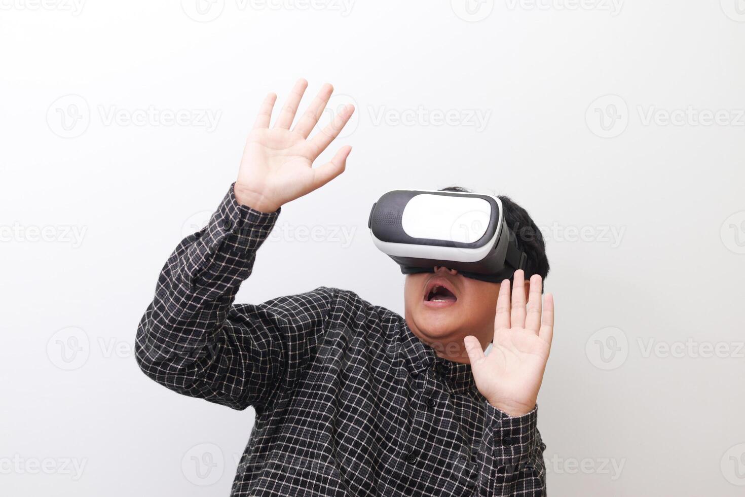 Portrait of Asian man in black plaid shirt using Virtual Reality VR glasses and protecting himself by spreading his arms from something big falling from above. Isolated image on white background photo