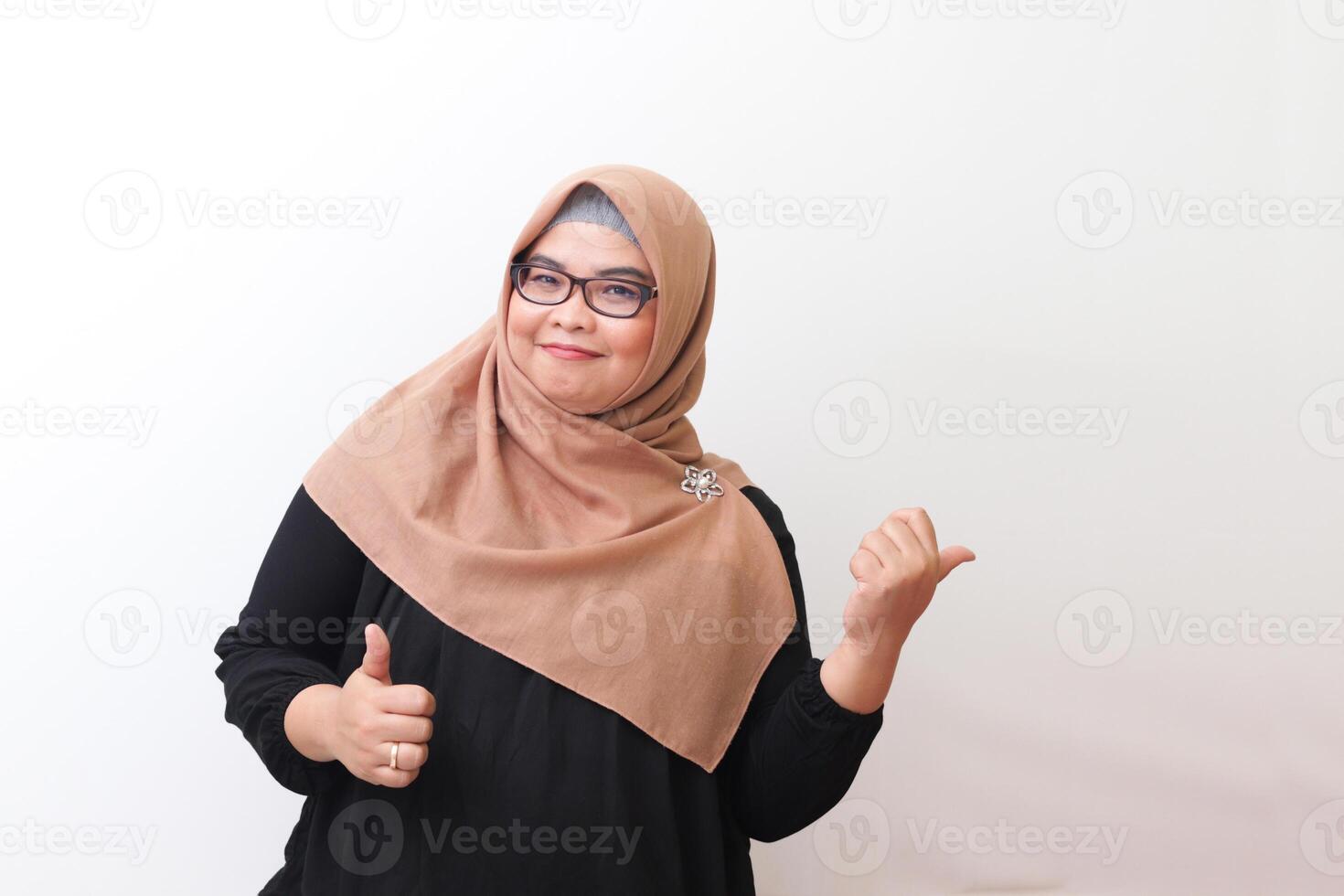 Portrait of cheerful Asian woman with hijab, making thumbs up hand gesture. Isolated image on white background photo