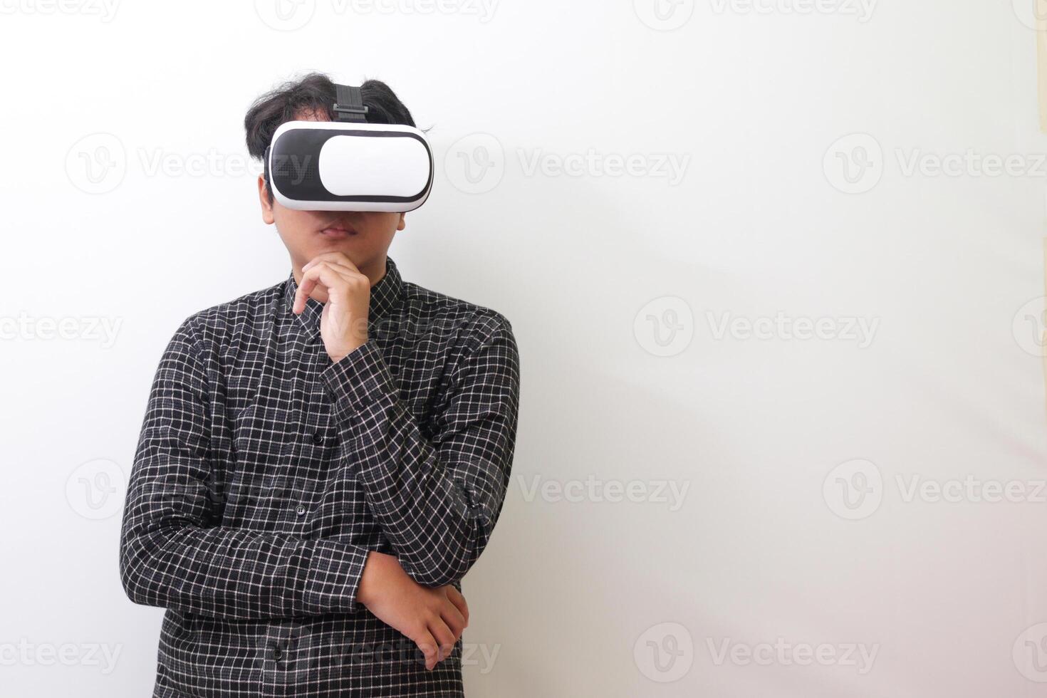 Portrait of Asian man in black plaid shirt using Virtual Reality VR glasses and thinking with hand on chin. Isolated image on white background photo