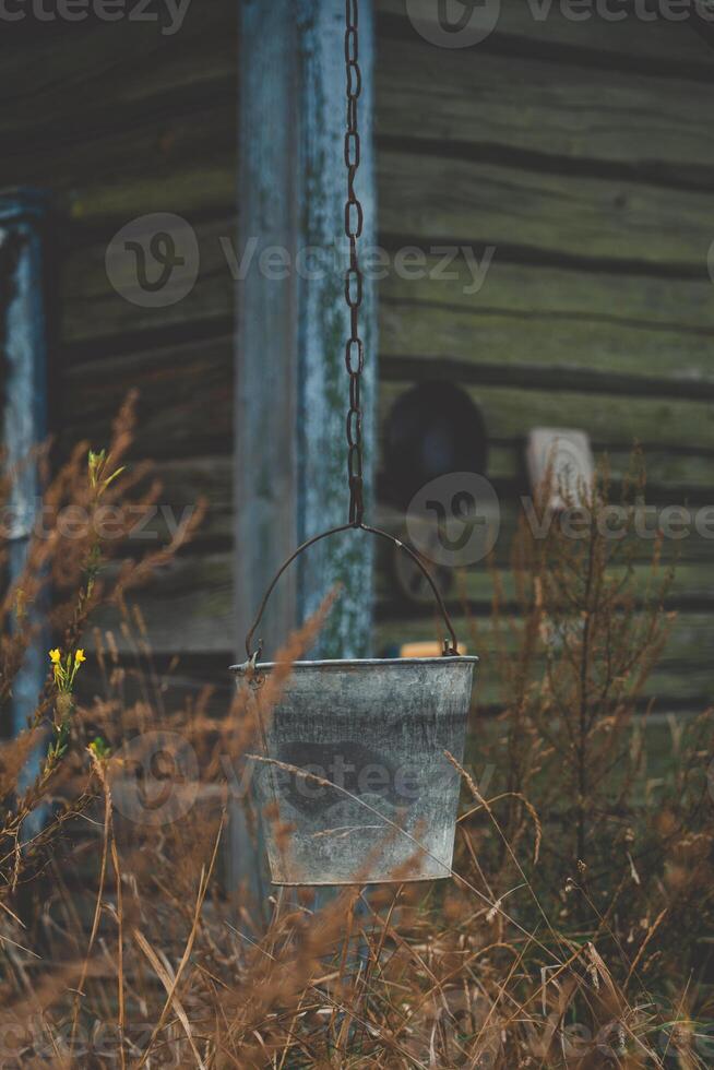 A bucket hangs on a chain against the background of an old, rustic house photo
