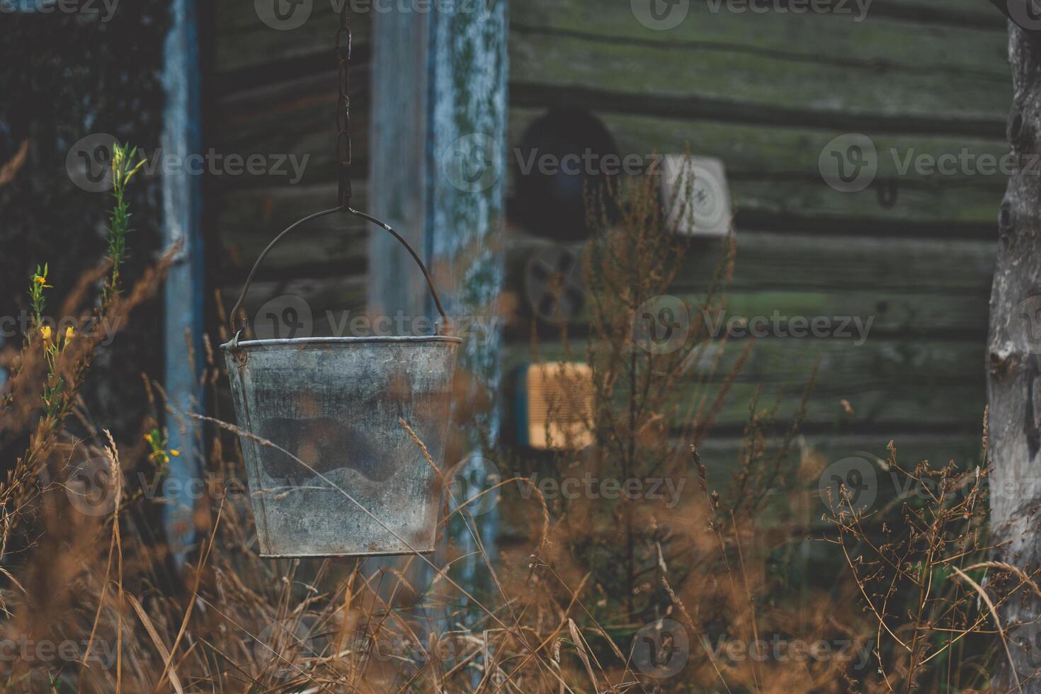 A bucket hangs on a chain against the background of an old, rustic house photo