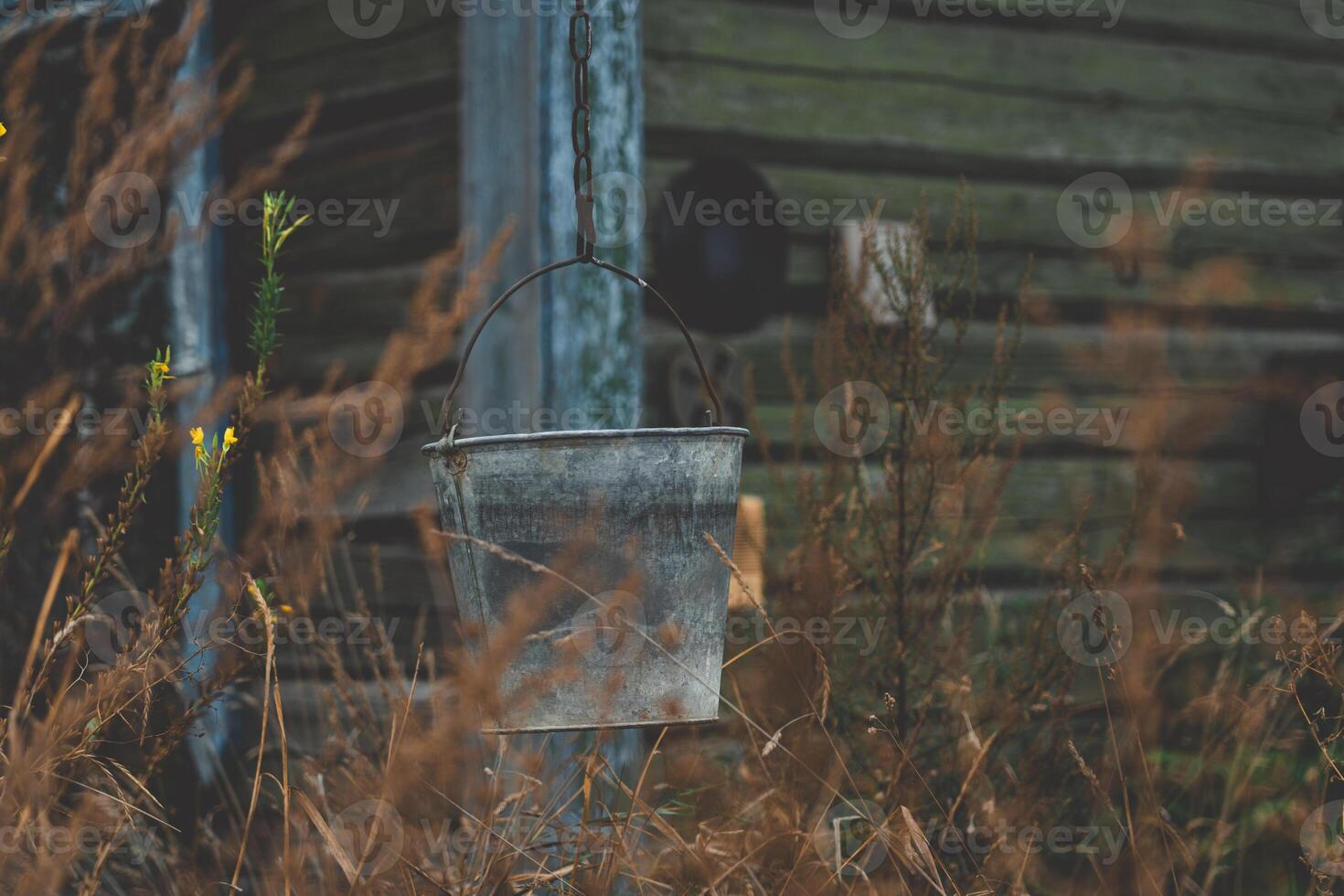 A bucket hangs on a chain against the background of an old, rustic house photo