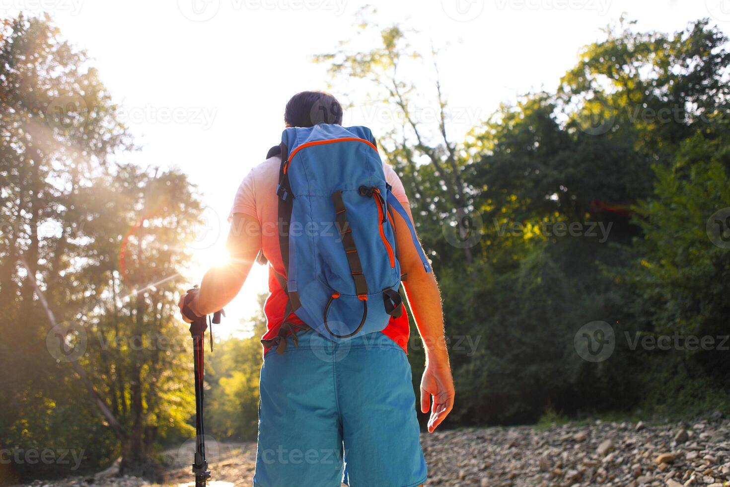 Man hiking with backpac and sticks in mountains in sunset photo