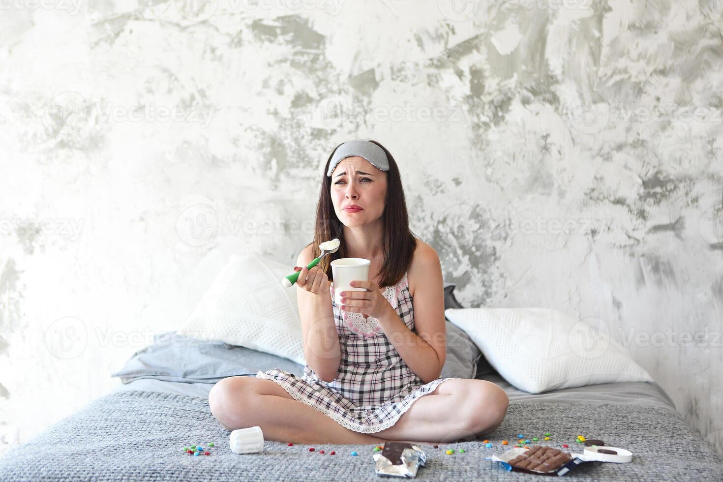 Cheerful sad young craing woman eating sweets in her bedroom photo