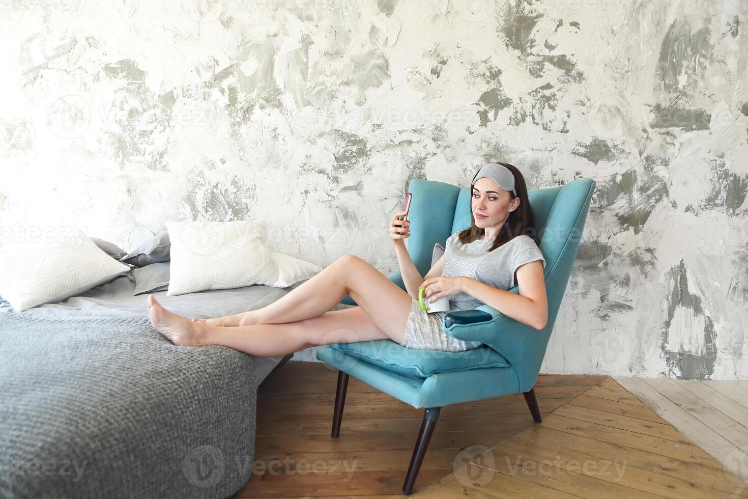 Beautiful young woman in the sleaping mask using mobile phone and drinking coffee photo