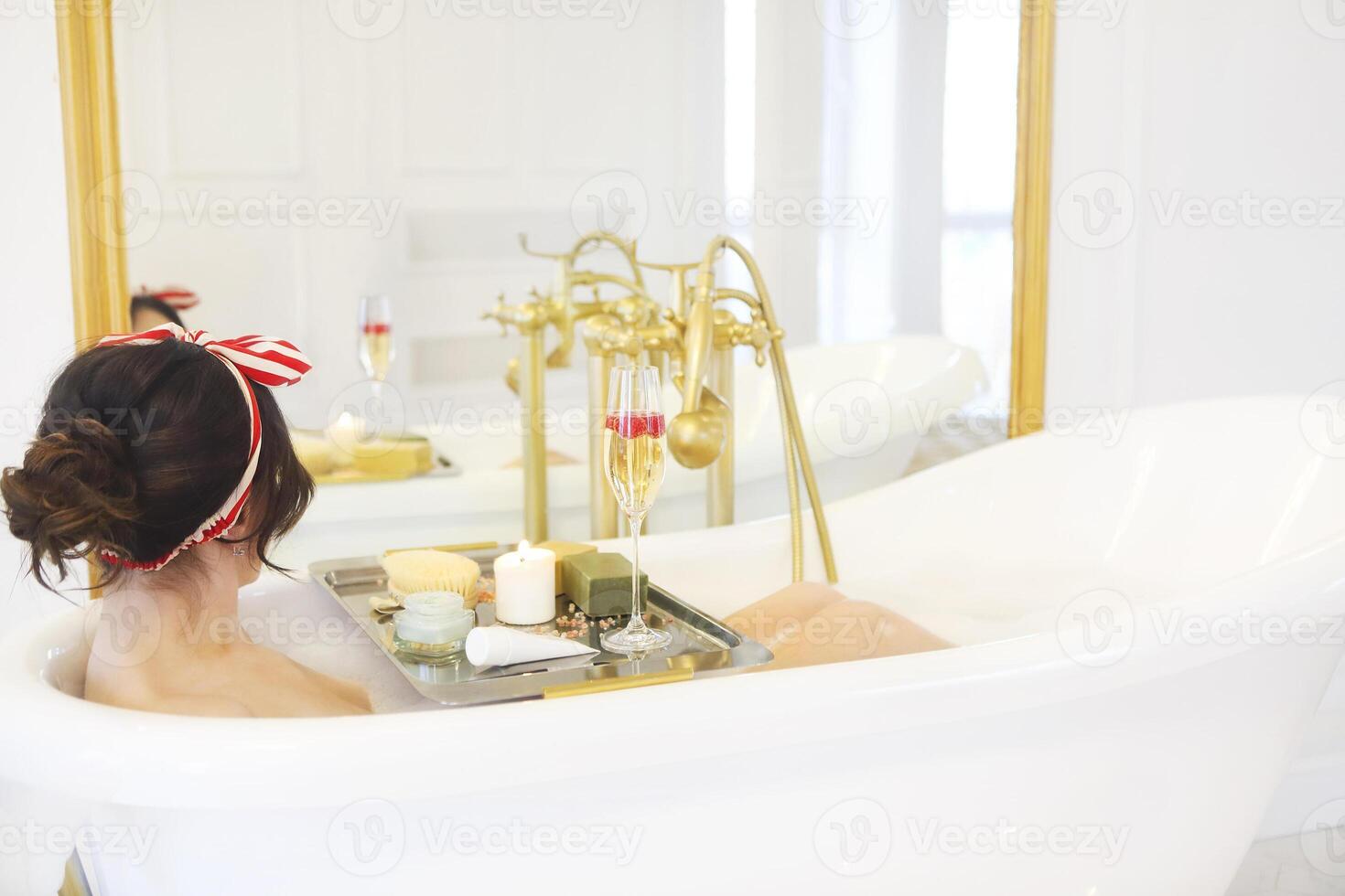 Attractive girl relaxing in bath on light background photo