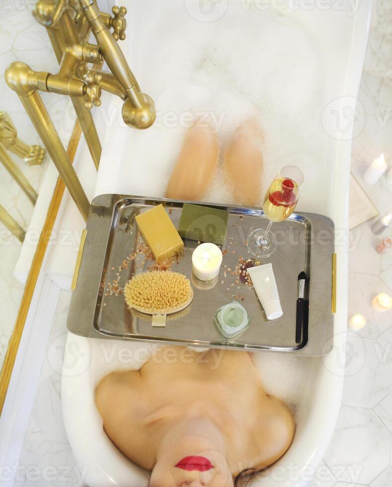 Attractive girl relaxing in the bath with tray of cosmetics photo