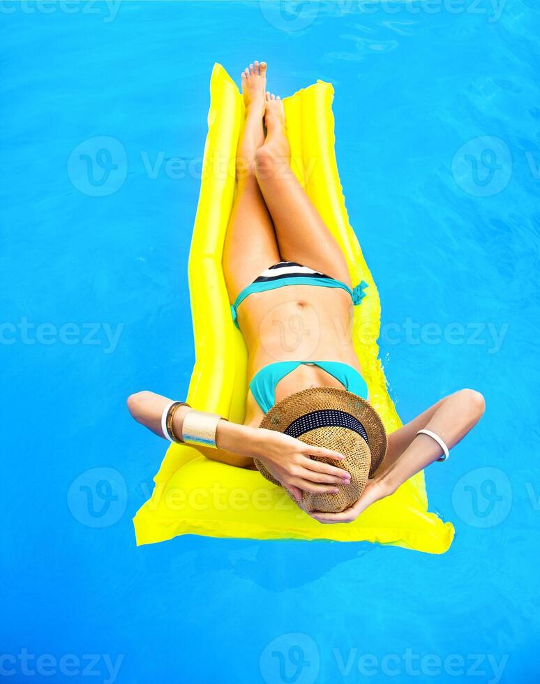 Young pretty woman with perfect tanned body lying on yellow air mattress photo