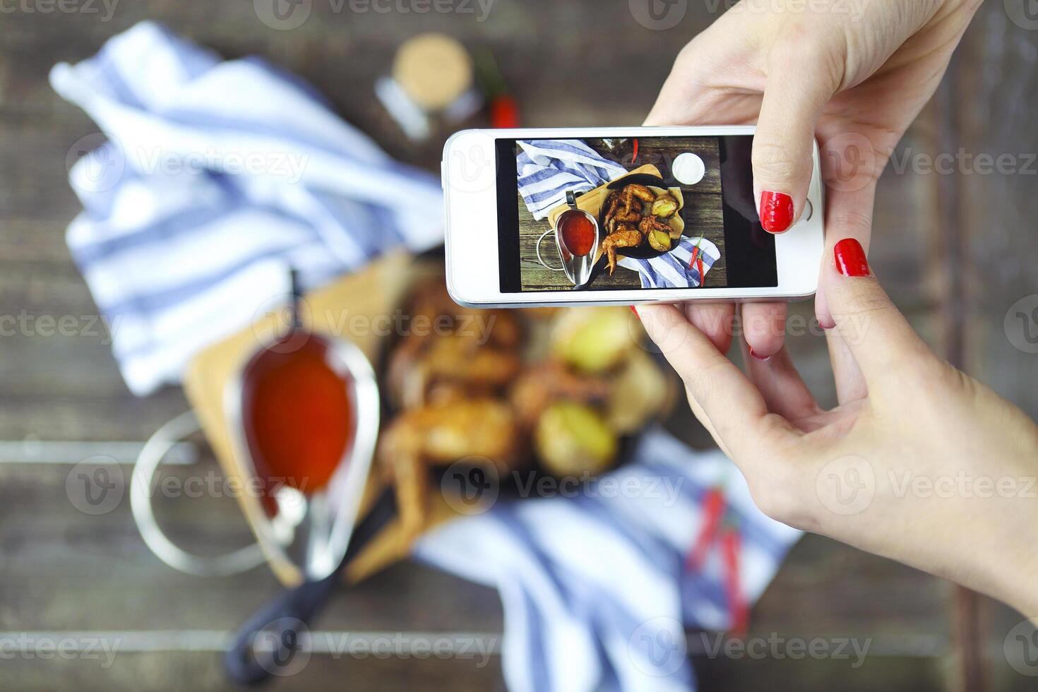 Woman taking a photo of a hot meat dishes on the wooden background with smaatphone
