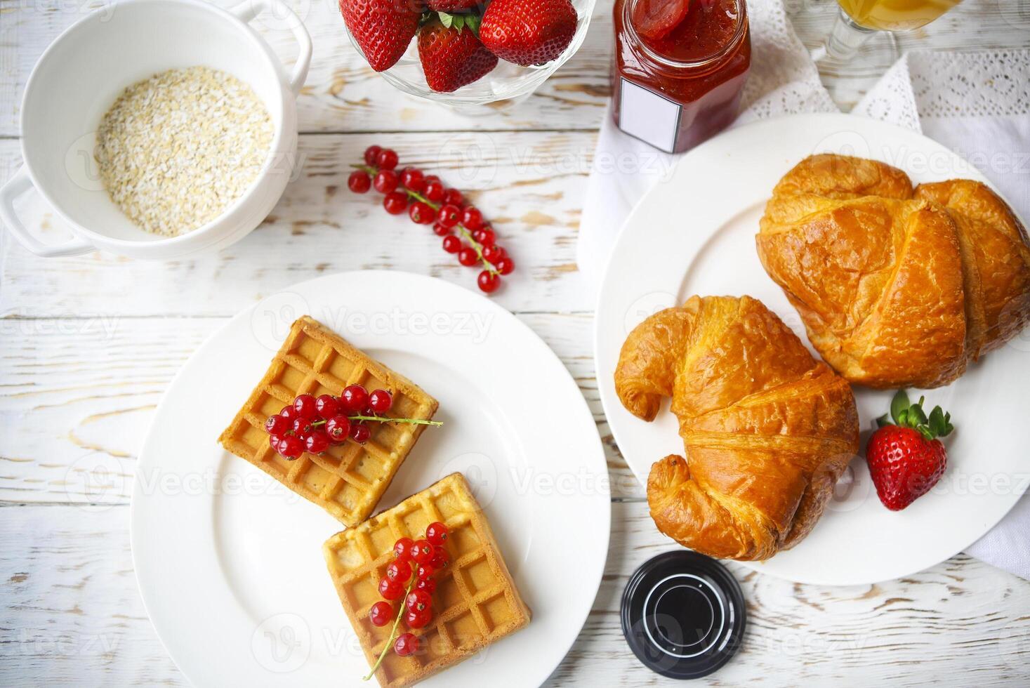 Waffles with red currant jam and berries, croissants, orange juice and oat flakes oatmeal photo