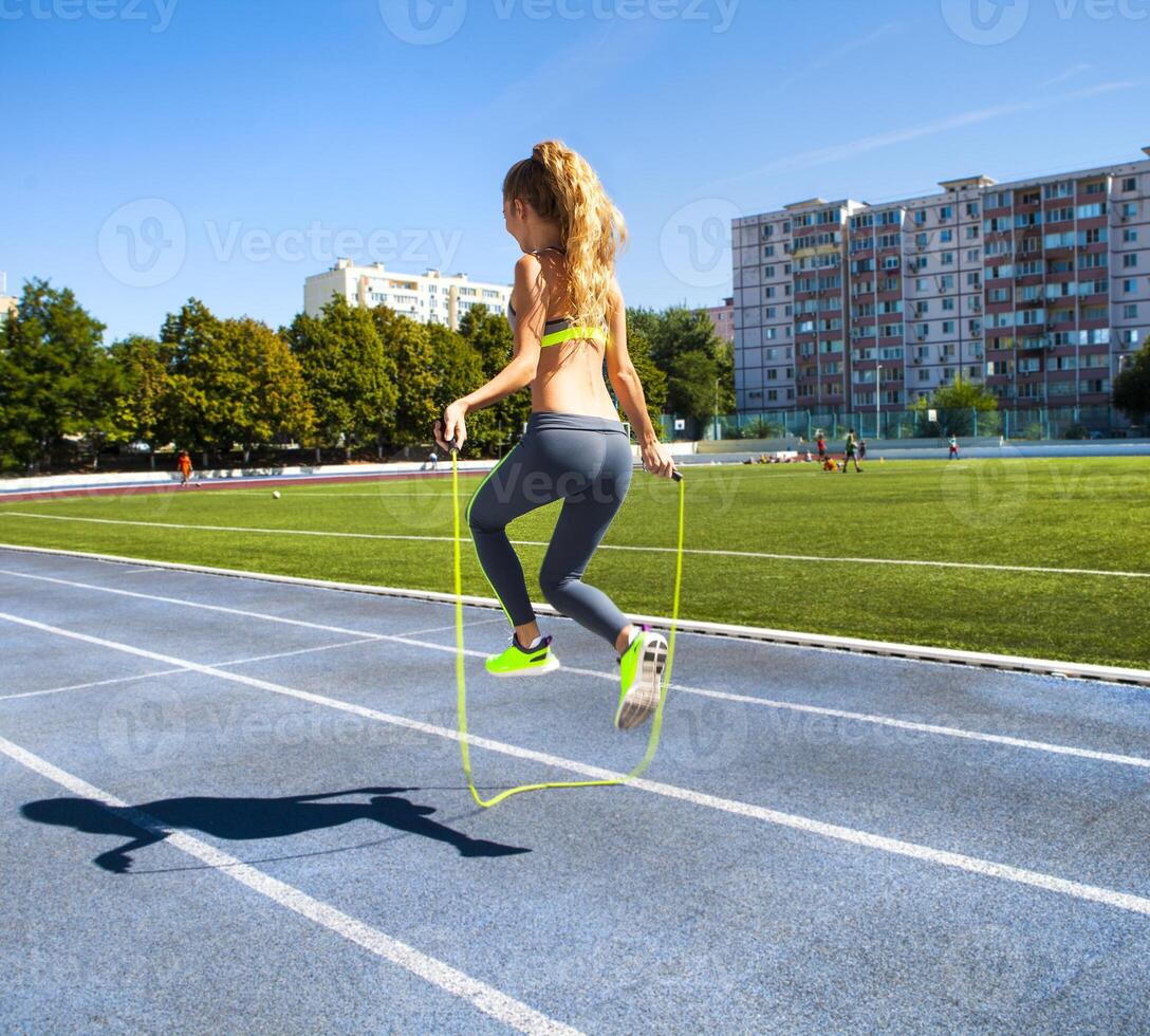 Young woman with a jumping rope in her hands with a stadium as background photo