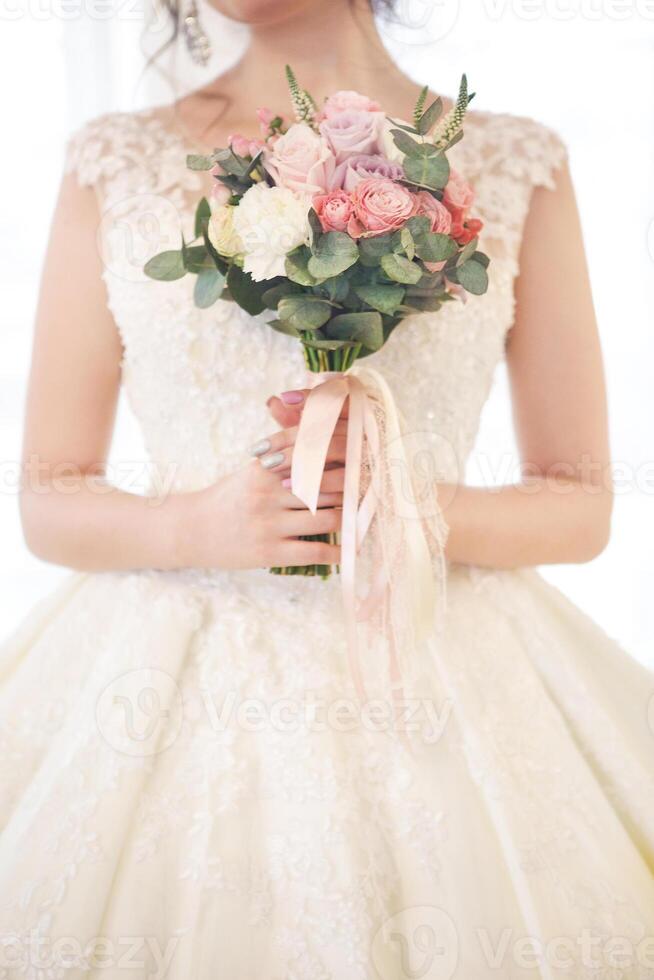 Young beautiful brunette woman with bouquet posing in a wedding dress photo