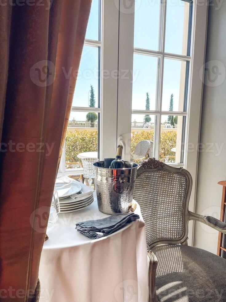 Table with white tablecloth, plates, napkins and ice cooler with dark glass bottle of wine. photo