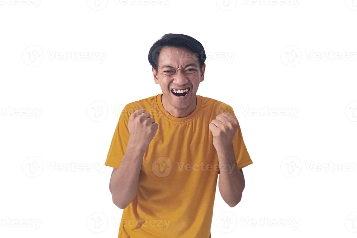 Handsome Asian man in a orange shirt raises both fists in a celebratory gesture, his face beaming with excitement and on white background emphasizes his triumphant and enthusiastic expression. photo