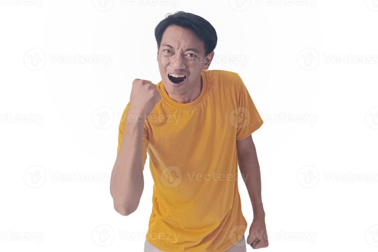Handsome Asian man in a orange shirt raises both fists in a celebratory gesture, his face beaming with excitement and on white background emphasizes his triumphant and enthusiastic expression. photo